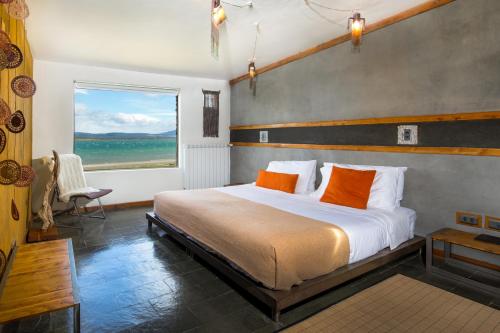 1 dormitorio con 1 cama con almohadas de color naranja y ventana en Hotel Altiplanico Puerto Natales en Puerto Natales