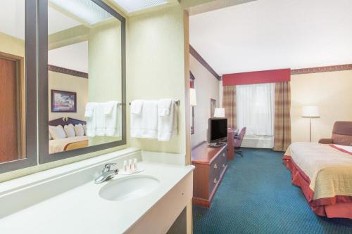 a hotel room with a bathroom with a bed and a sink at Baymont by Wyndham Jonesboro in Jonesboro
