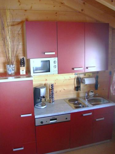 a kitchen with red cabinets and a sink and a microwave at Postalm Lodge in Seidegg