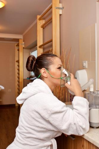 a woman standing at a kitchen counter drinking from a mixer at Balneo Complex & Spa Aquatonik in Velingrad