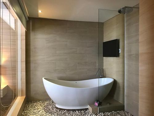a bath tub in a bathroom with a glass wall at Crystal Lotus Hotel Yogyakarta in Yogyakarta