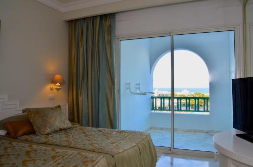 a bedroom with a bed and a large glass window at Royal Garden Palace - Families and Couples in Midoun