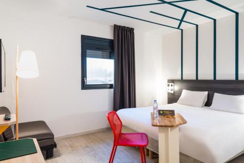 a hotel room with a bed and a red chair at ibis Styles Rouen Val De Reuil in Val de Reuil