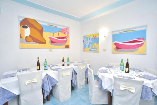 a restaurant with white tables and white chairs and paintings at Charme Hotel La Villa Tina in Ischia