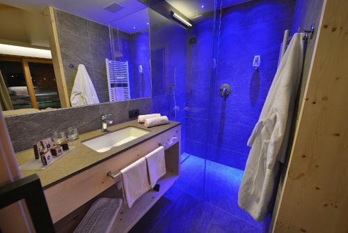Hotel Roberta Alpine Adults only في ليفينو: حمام مع حوض ودش مع اضاءة زرقاء