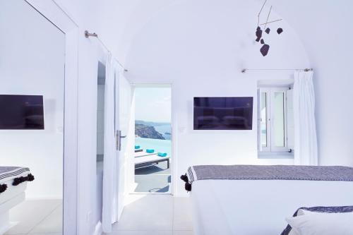 a white bedroom with two beds and a view of the ocean at Cosmopolitan Suites - Small Luxury Hotels of the World in Fira