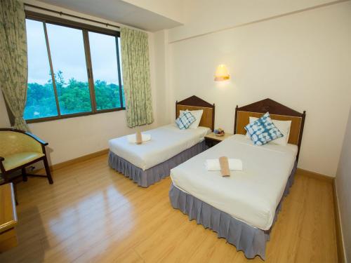 a room with two beds and a chair and a window at Phrae Nakara Hotel in Phrae