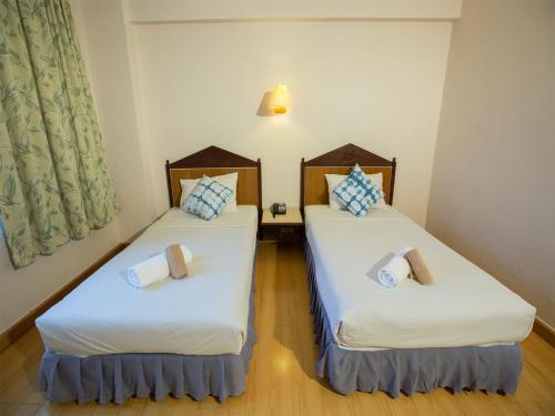 two beds in a room with white sheets and blue pillows at Phrae Nakara Hotel in Phrae