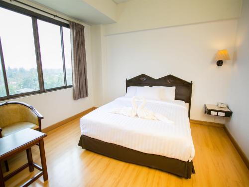 a bedroom with a bed and a desk and windows at Phrae Nakara Hotel in Phrae
