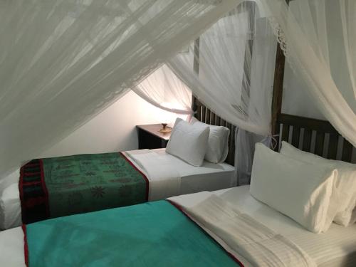 two beds in a room with white curtains at Khalid's Guest House in Galle