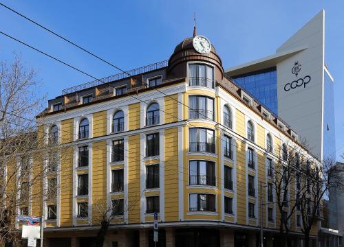 a yellow building with a clock on top of it at Hotel COOP, Sofia in Sofia