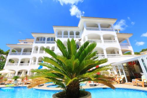 a large white building with a palm tree in front of it at Atalaya Bosque Apartamentos in Paguera