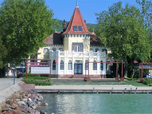 a large white house with a red roof next to the water at Aqua Apartman in Révfülöp