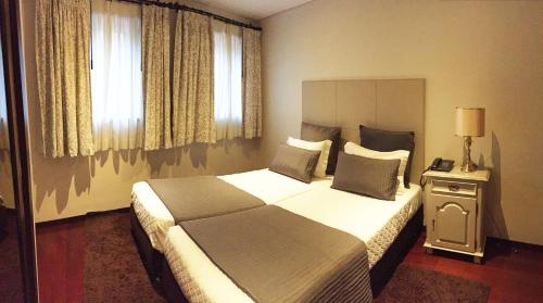 um quarto de hotel com uma cama grande e janelas em Hotel Central Jardim no Gerês