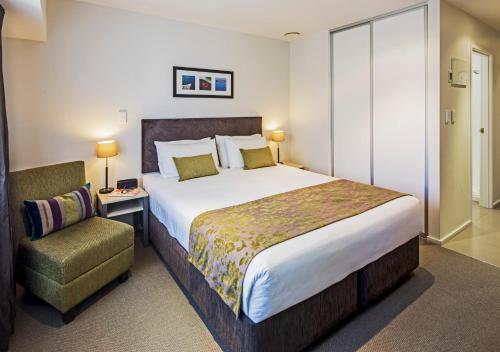 a bedroom with a large bed and a chair at Quest Albany Serviced Apartments in Auckland