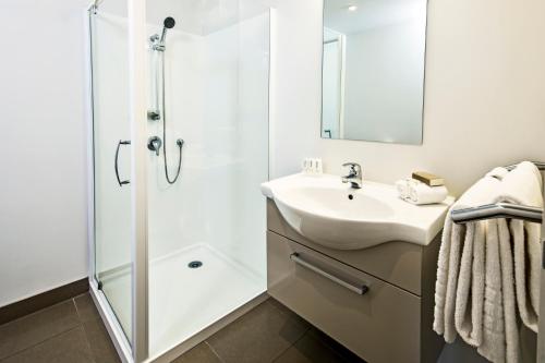 a bathroom with a shower, sink, and mirror at Quest Albany Serviced Apartments in Auckland