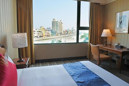 a hotel room with a bed and a desk and a window at Wei-Yat Grand Hotel in Anping