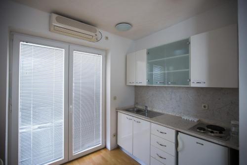 una cocina con armarios blancos y una ventana con ventilador en Apartments Peris Resort, en Novalja