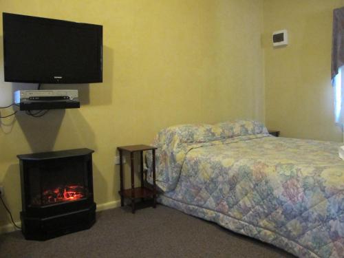 Cedar Lodge Cabins في جبل فيكتوريا: غرفة نوم بسرير وتلفزيون ومدفأة