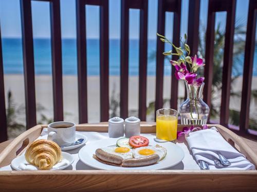 Een ontbijtplateau met eieren en brood op een tafel met uitzicht op het strand. bij Sandy Beach Non Nuoc Resort in Da Nang