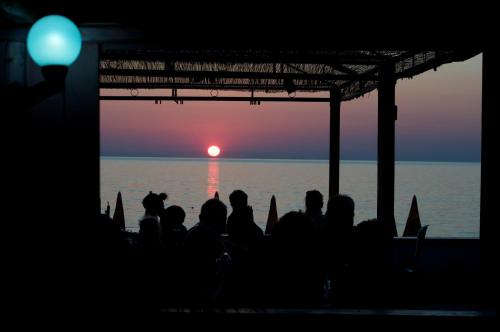 a group of people sitting on a beach watching the sunset at Hotel Villa Smeraldo in Orbetello