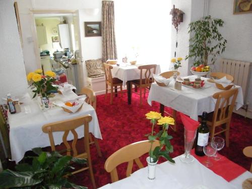 a dining room with tables and chairs with flowers on them at El Tabora Guest House in St. Peter Port