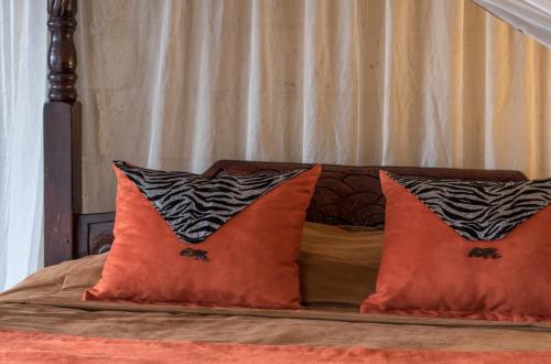 a bed with two orange pillows on top of it at Rhino Watch Safarilodge in Mweiga