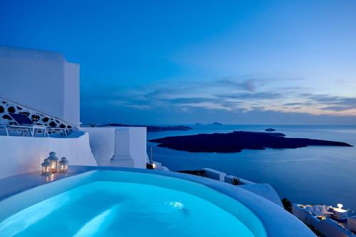 a blue swimming pool at night with the ocean at Nautilus Villa in Firostefani