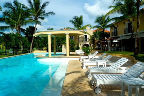 una piscina con tumbonas blancas junto a un edificio en The Golf Suites, en Punta Cana