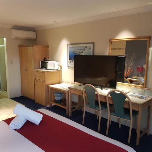 a room with a desk with a television and chairs at Chelsea Motor Inn in Coffs Harbour
