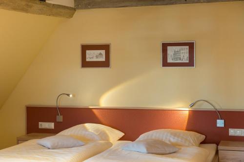 two beds in a room with two lamps on the wall at Hotel Theophano in Quedlinburg