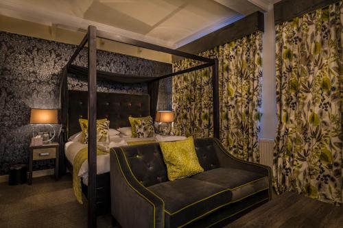 a bedroom with a four poster bed with a couch at The Royal Oak Hotel, Welshpool - The Coaching Inn Group in Welshpool