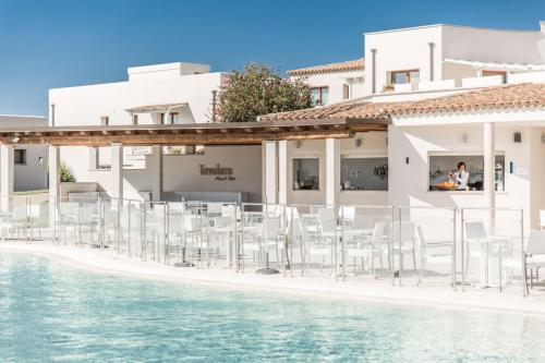 a row of white chairs on a beach next to a building at Grande Baia Resort & Spa in San Teodoro