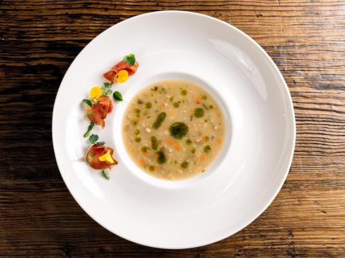 a bowl of soup on a white plate on a table at Hotel Riederhof- Urlaub mit WAU! in Ried im Oberinntal