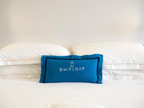 a blue pillow sitting on a bed with white pillows at White Bay in Fontane Bianche