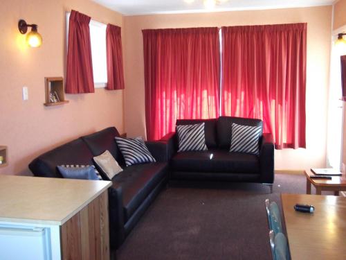 a living room with a black couch and red curtains at Belle Bonne Motel in Christchurch