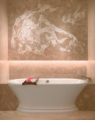 a bath tub in a bathroom with a painting on the wall at Raffles Jakarta in Jakarta