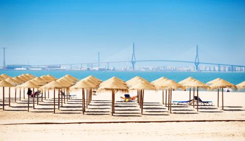 a group of straw umbrellas on a beach at Hotel Puerto Bahía & Spa in El Puerto de Santa María
