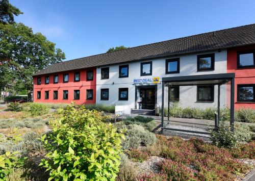 a red and white building with plants in front of it at Best Deal Airporthotel Weeze in Weeze