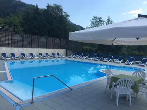 a swimming pool with chairs and a table and an umbrella at Hotel Scaranò in Levico Terme