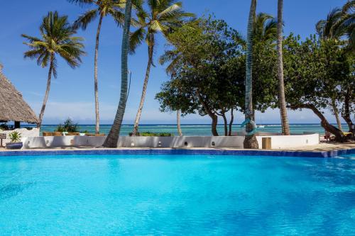 a swimming pool with palm trees and the ocean in the background at Ocean Village Club (Adults Only) in Diani Beach