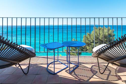 a balcony with two chairs and a blue table and chairs at Hôtel Le Bailli De Suffren in Rayol-Canadel-sur-Mer