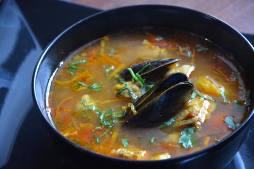 a black bowl of soup with mussels in it at Hotel Cesarski - Kaiserhof in Giżycko