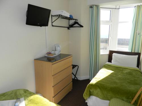 a room with two beds and a dresser with a television at Ocean Bay in Blackpool