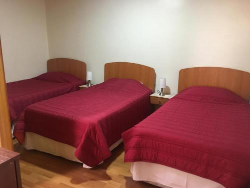 two beds in a room with red sheets at Hostería Estelita in Panimávida