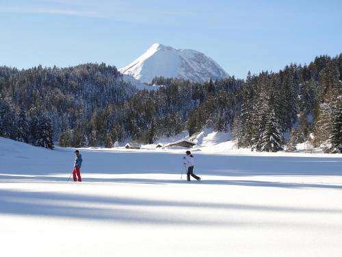 two people walking in the snow with a mountain in the background at Hotel Tirolerhof in Leutasch