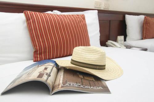 a hat sitting on top of a bed with a book at Hotel Residencial in Mérida