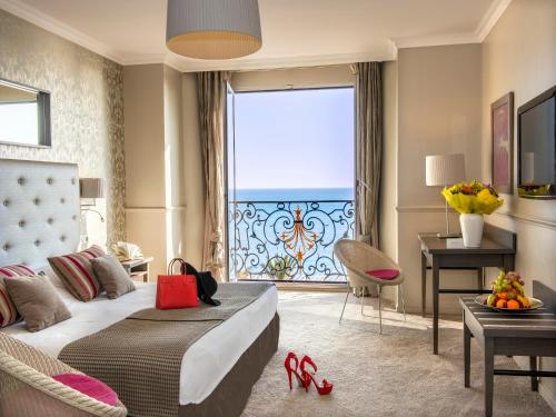 ニースにあるオテル ル ロワイヤル プロムナード デ ザングレのベッドと大きな窓が備わるホテルルームです。