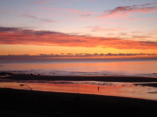 a sunset over the ocean with a person walking on the beach at Ocean Front East End Beach House in New Plymouth