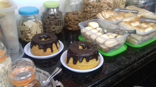 three cakes on plates on a counter with jars of food at Hotel Royal Class in Guaratinguetá